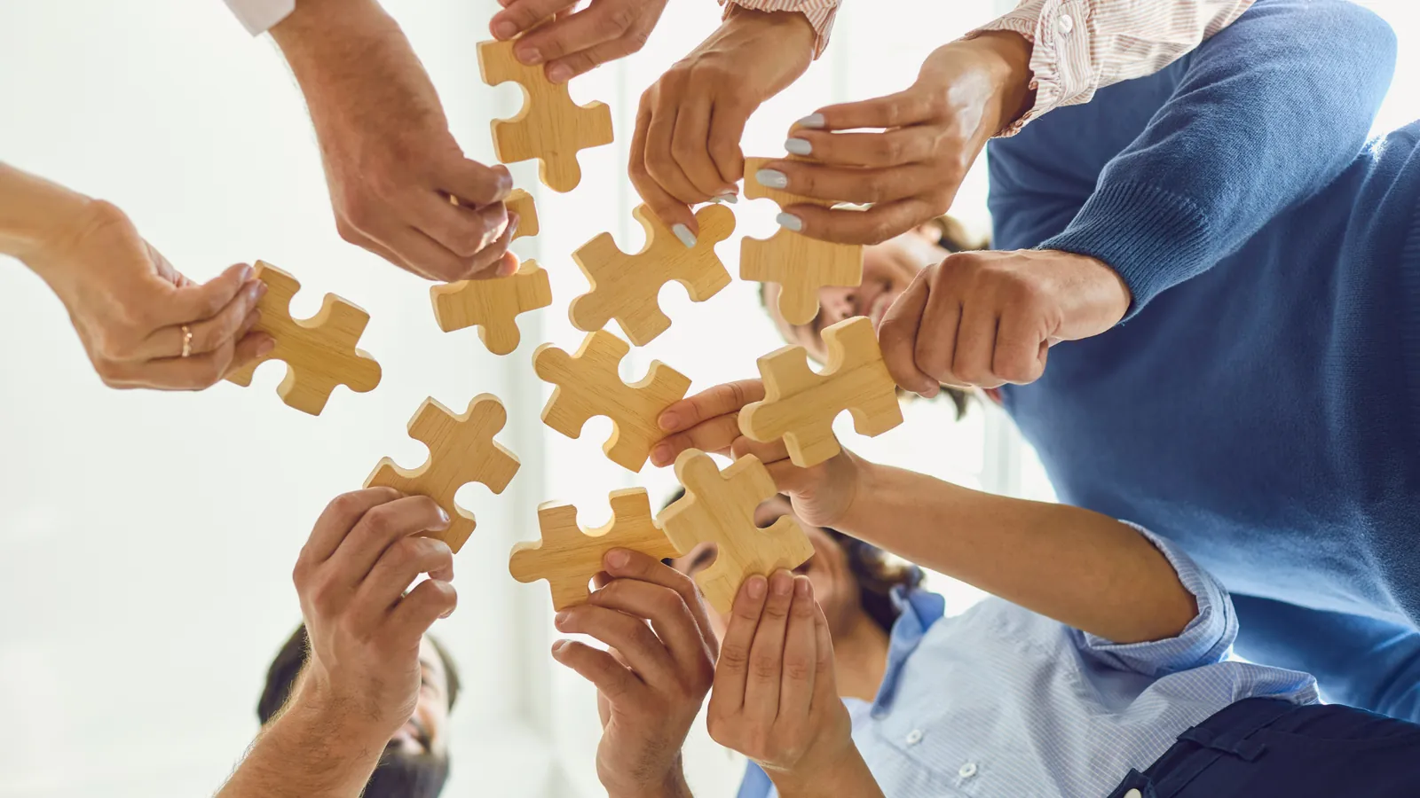 Several people holding jigsaw pieces and fitting them together.