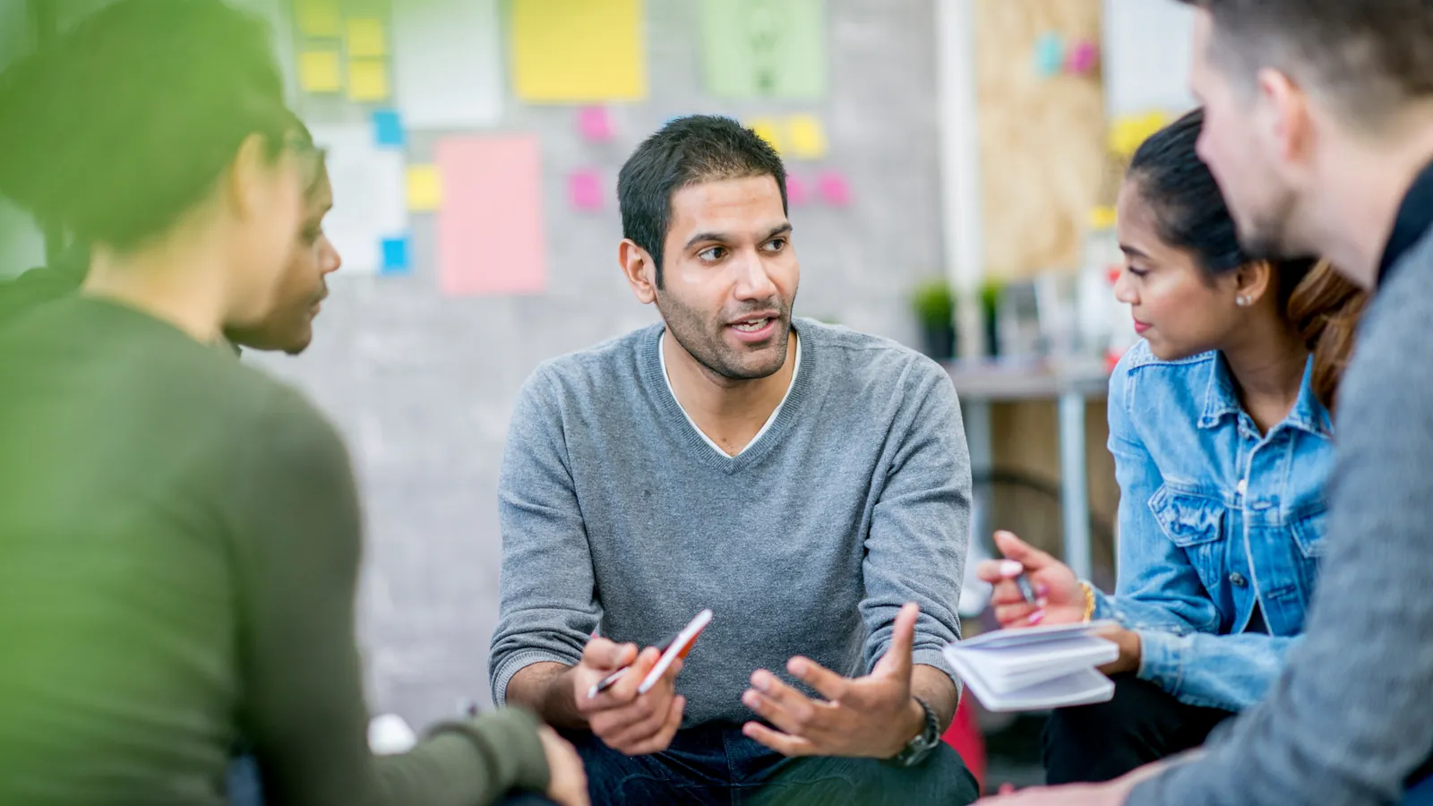 A team talking through a plan in front of a wall of sticky notes.